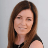 Sian Kelly owner growing accounting business with straight brown hair and a black top smiles at the camera in front of a plain light background.